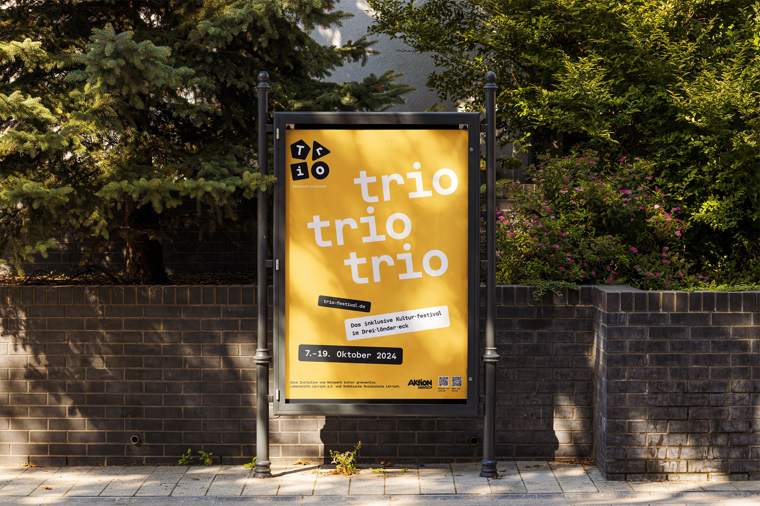 Gelbes TRIO-Festival Plakat vor bewachsener Wand